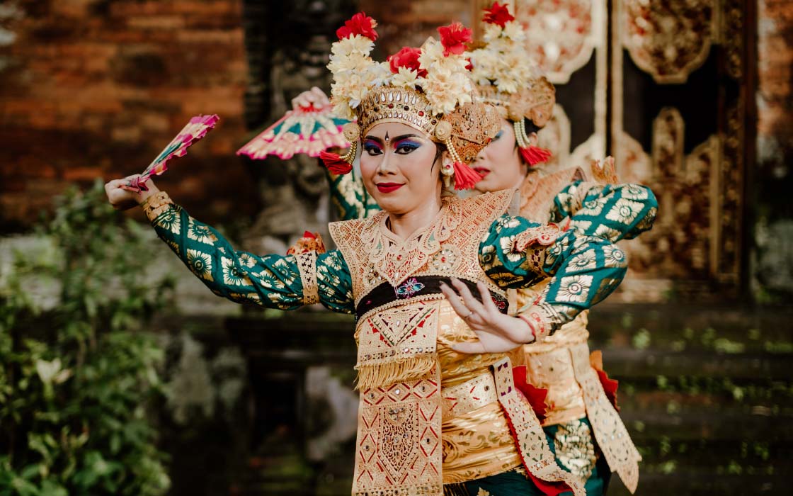 Zwei Frauen tanzend, die ein traditionelles indonesisches Gewand tragen, mit Blumen auf dem Kopf und einem Fächer in der Hand