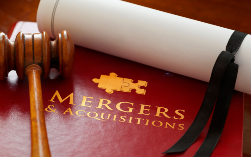 Mergers and Acquisitions Inschrift auf einer roten Pappe. Darauf ein Richterhammer und eine Papierrolle